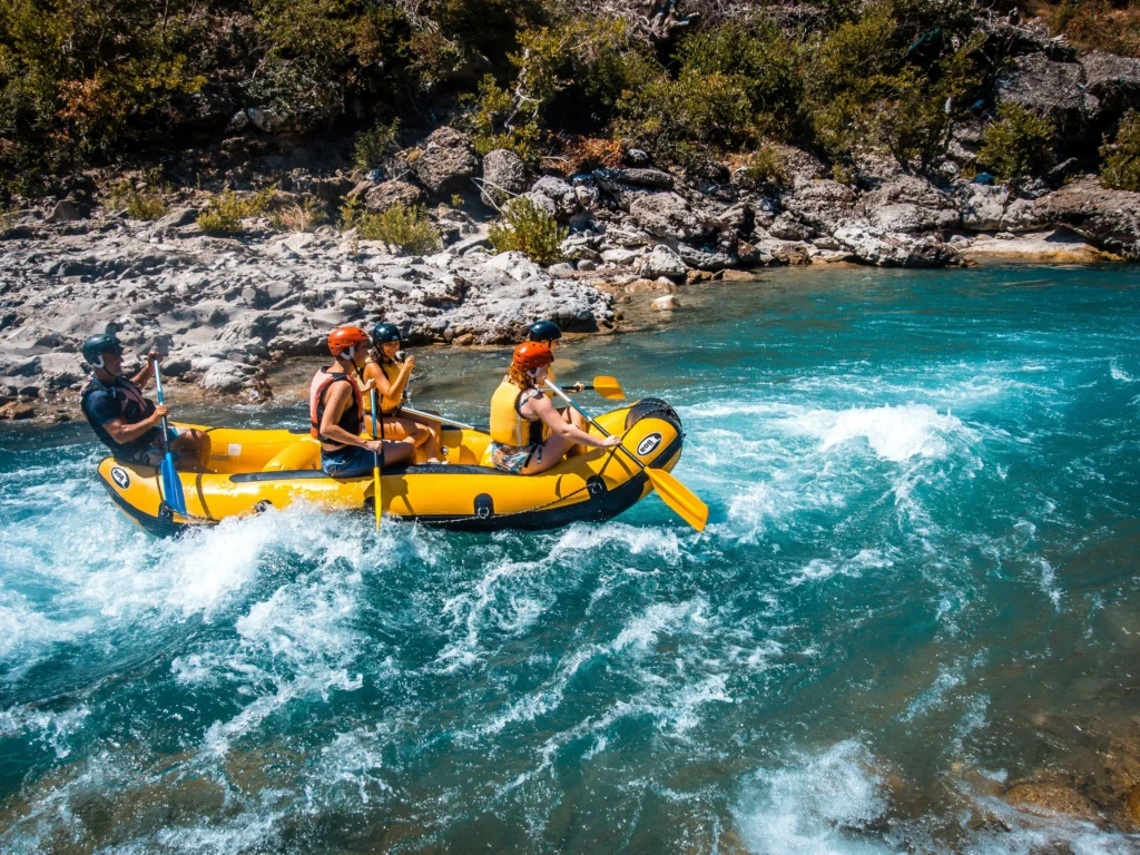 In the image, a rafting inflatable boat on a river, with five people on board paddling.