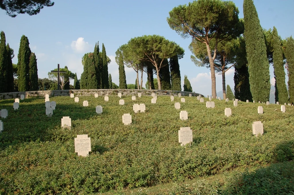 Immagine del cimitero militare di Cassino: si vede un prato con numerose lapidi bianche, uguali tra loro, e attorno molti alberi.