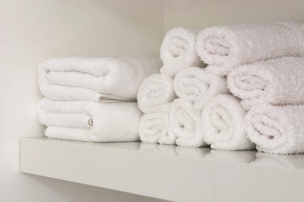 Image of several white towels rolled up and placed on a white shelf.