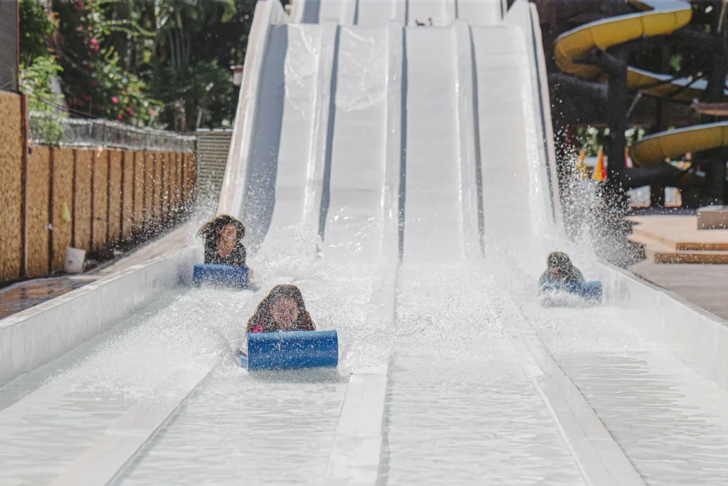 Image of a four-lane water park slide, with three children in the foreground sliding down simultaneously.