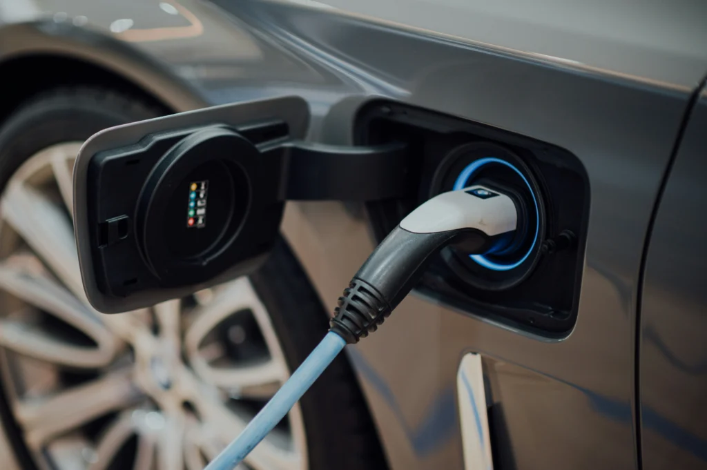 In the image, a close-up of a charging connector plugged into a gray electric car.